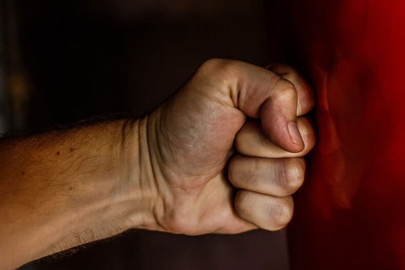 A fist punching a red boxing heavy bag.