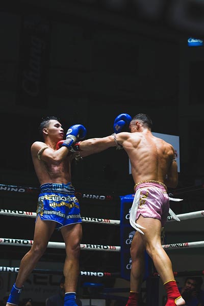 Two Muay Thai fighter in Blue and Pink shorts exchange blows.
