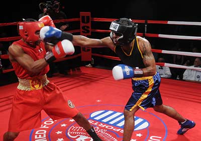 Two boxers exchange blows in the ring a fighter in red blocks a punch.