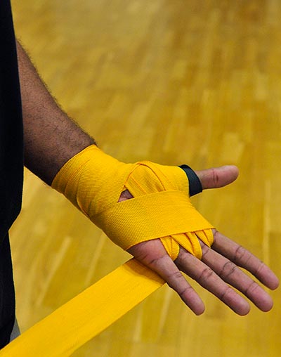 Some yellow hand wraps are being put on by a boxer before he begins sparring.