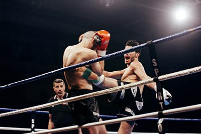 A fighter in black shorts lands a hard left kick to the body of his opponent.