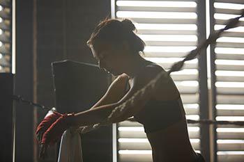 A woman boxer rests on the ropes in the boxing gym.